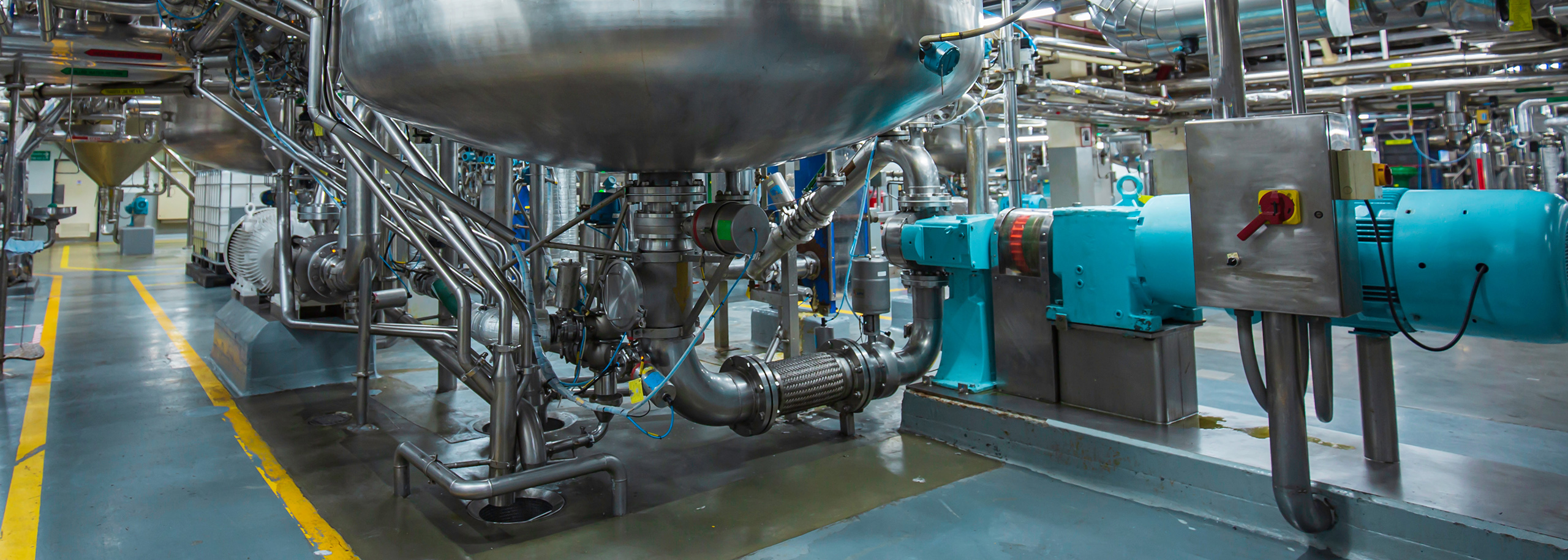 Siloanlage mit angeschlossenen Rohrleitungen – Symbolbild für Sondermaschinenbau in der Nahrungsmittelindustrie Unterer Teil eines Edelstahltanks mit angeschlossenen Rohrleitungen und Pumpe in einer Produktionshalle – Symbolbild für Verbindungslösungen und Sondermaschinenbau der Stahlberg GmbH in der Nahrungsmittelindustrie.