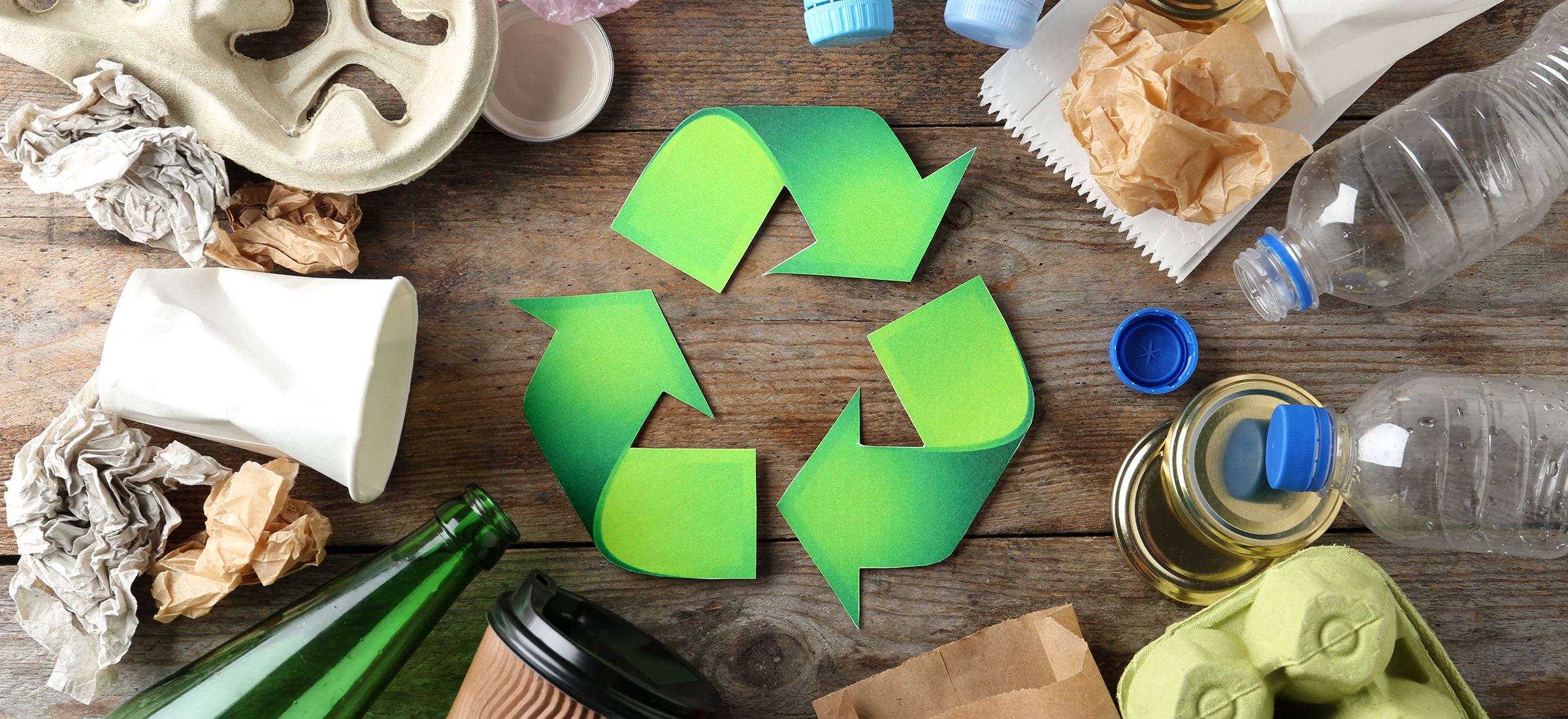 Stahlberg sucht kontinuierlich nach umweltfreundlichen Alternativen zu Plastik Grünes Recycling-Symbol, umgeben von verschiedenen leeren Verpackungen aus Papier, Glas und Kunststoff – Symbolbild für das Engagement von Stahlberg, den Einsatz von Plastik zu vermeiden und nachhaltige Alternativen zu fördern