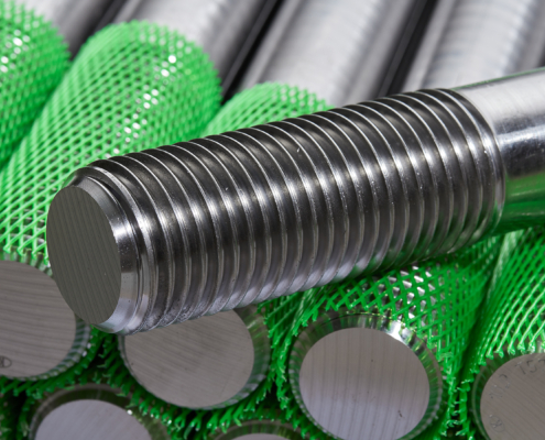 Sonder-Drehteile Stapel von präzise gefertigten Metall-Gewindebolzen aus der Produktion der Stahlberg GmbH in Langenfeld – mit grünem Schutznetz für sicheren Transport und Lagerung.