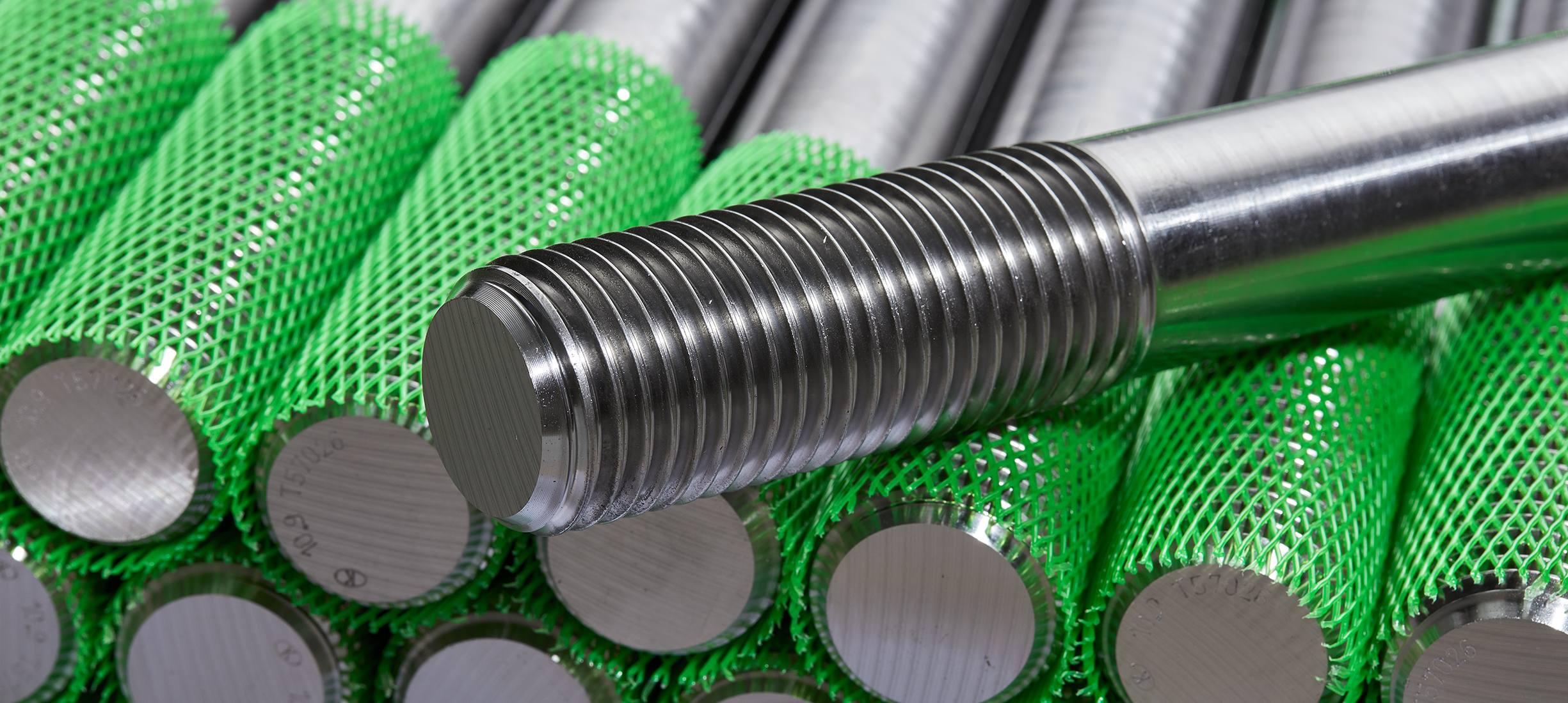 Sonder-Drehteile Stapel von präzise gefertigten Metall-Gewindebolzen aus der Produktion der Stahlberg GmbH in Langenfeld – mit grünem Schutznetz für sicheren Transport und Lagerung.